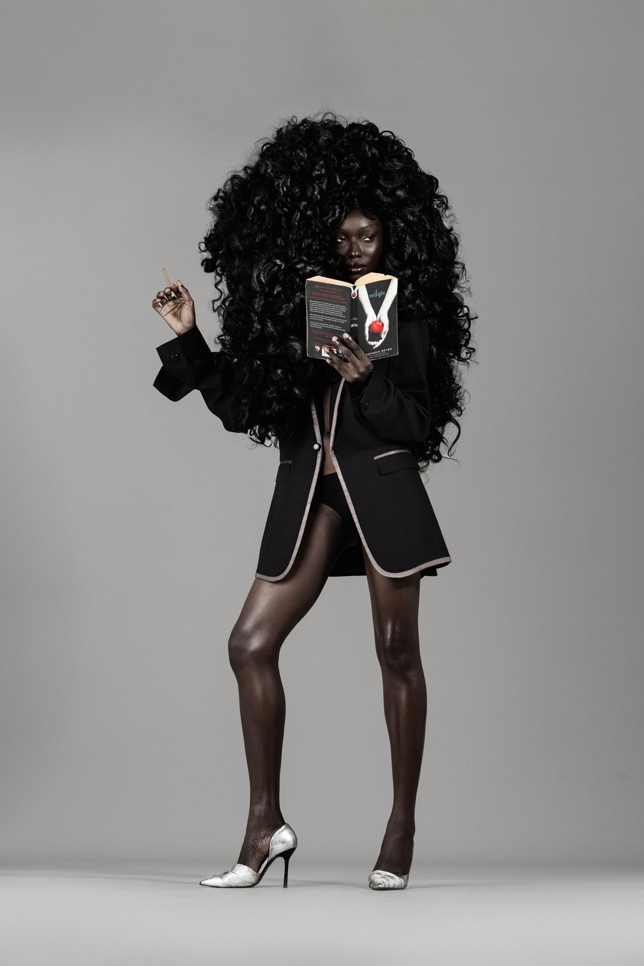 Full-length portrait holding a Twilight book in black tailoring and silver heels