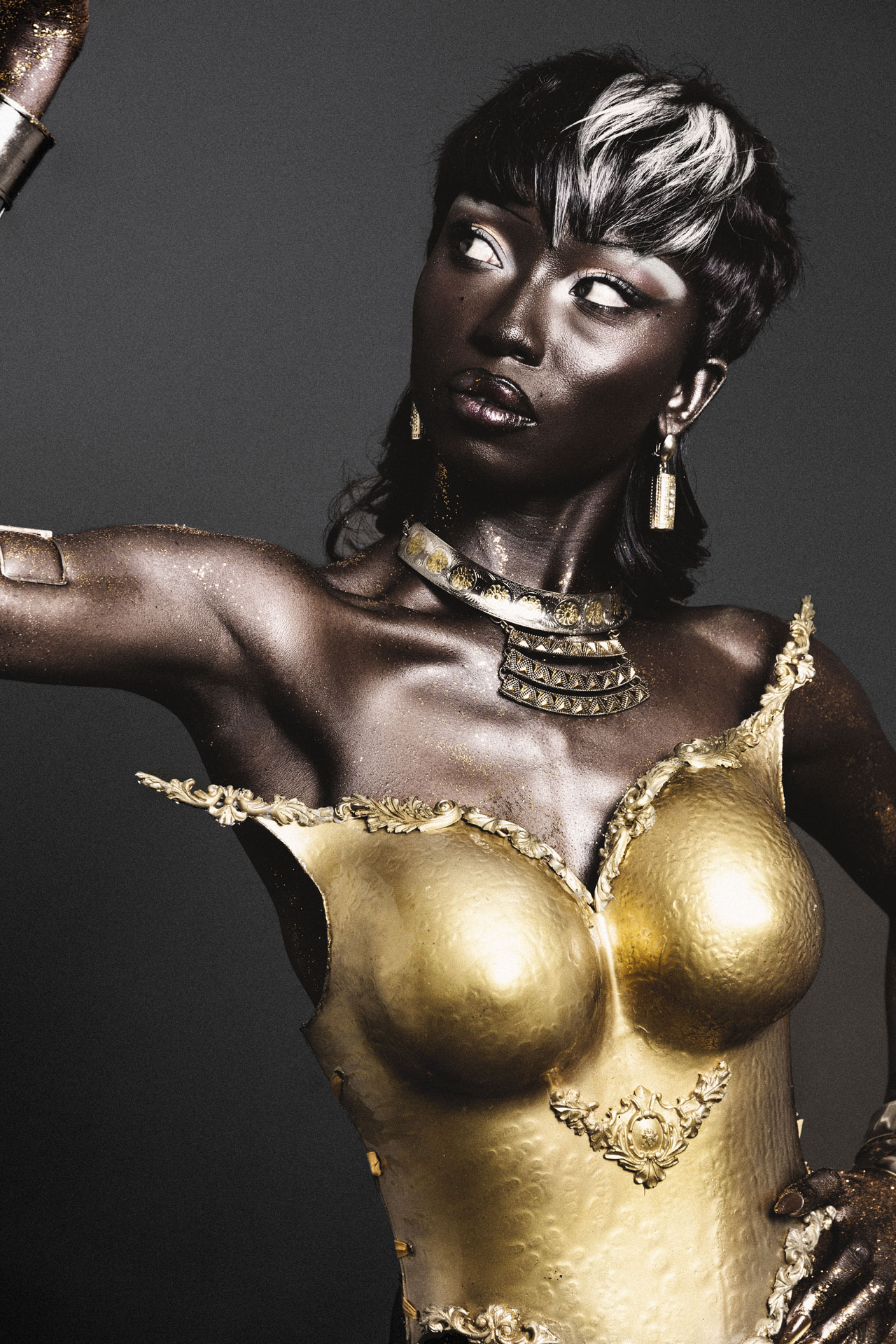 Black Twilight portrait with a sculpted gold bodice and raised arm against charcoal