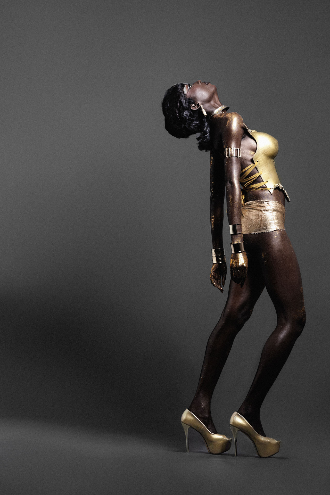 Full-length arched side profile in a gold bodice and gold heels
