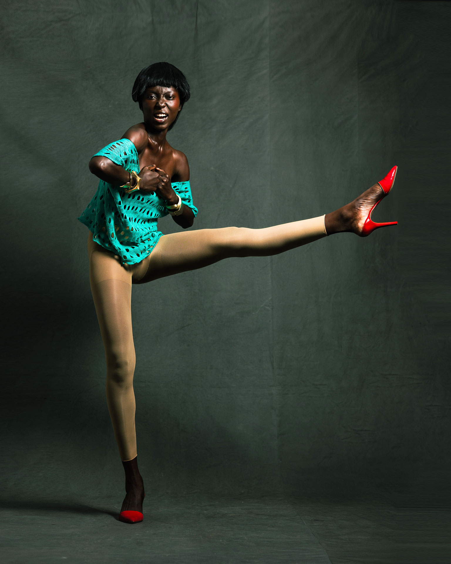 Full-length studio pose with one leg raised, wearing red heels