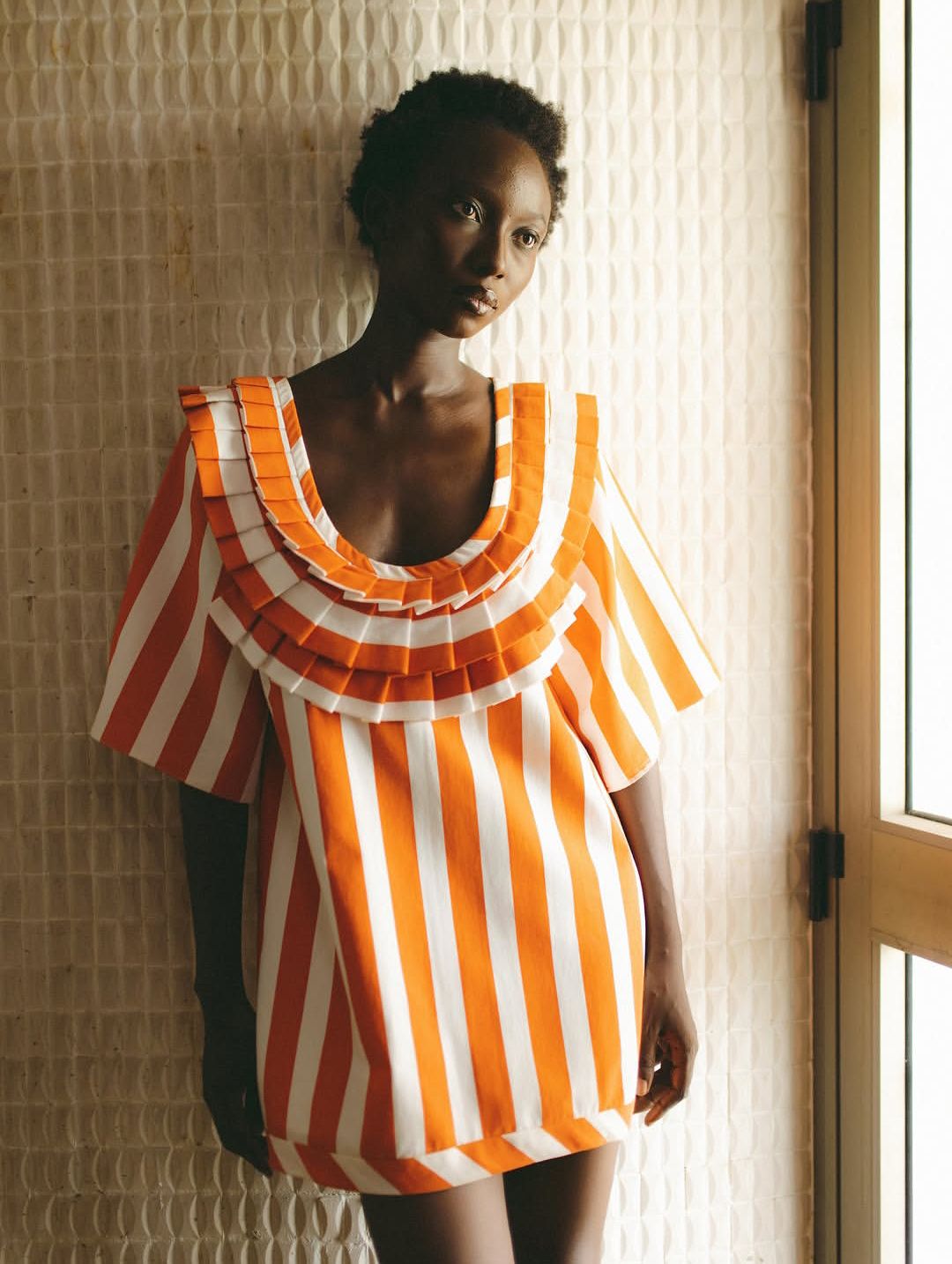 Orange-and-ivory campaign portrait against patterned curtains
