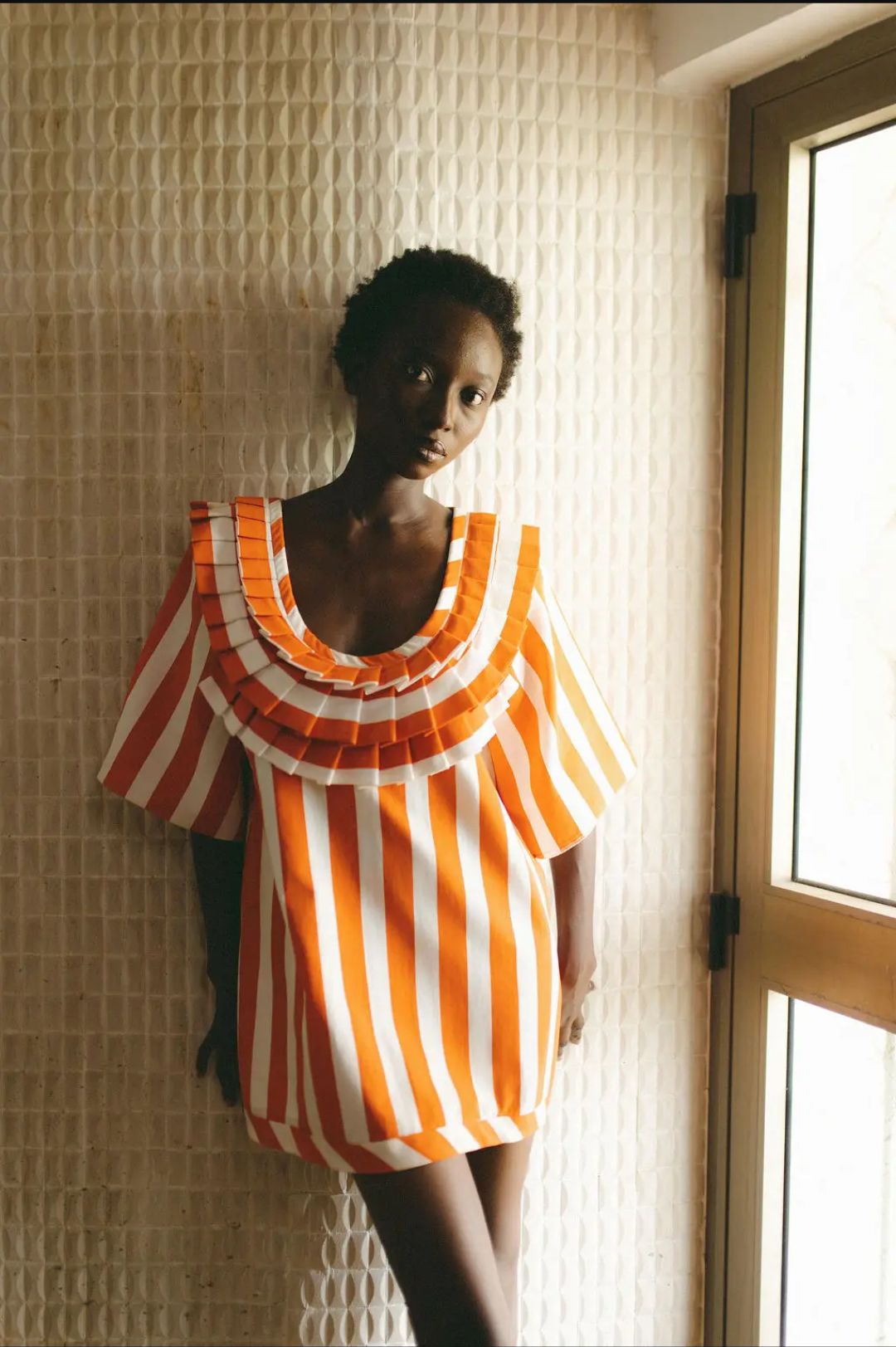 Oríré campaign portrait in orange-and-ivory pleats
