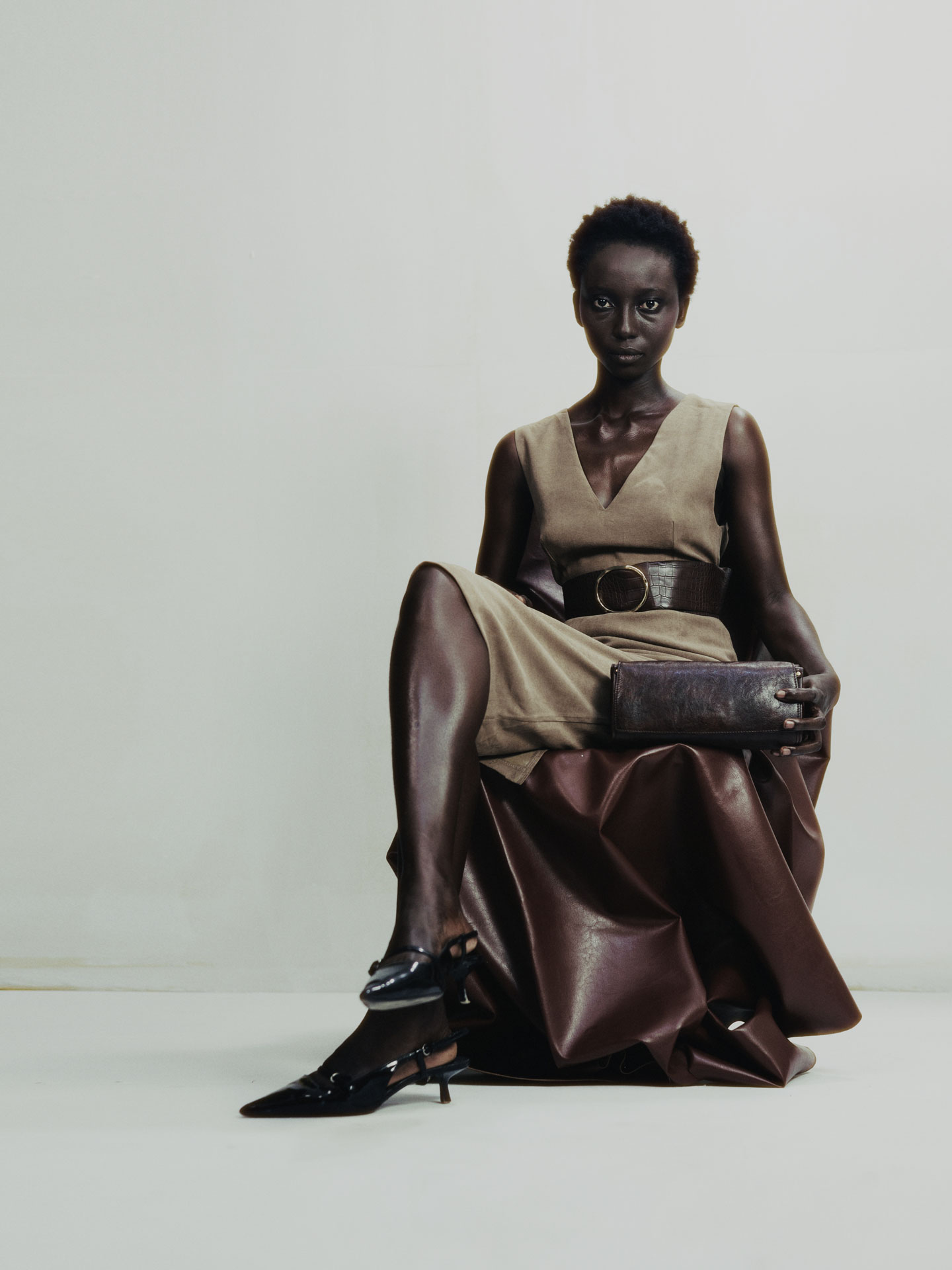 Seated full-length studio test in taupe layers, a wide belt and pointed boots